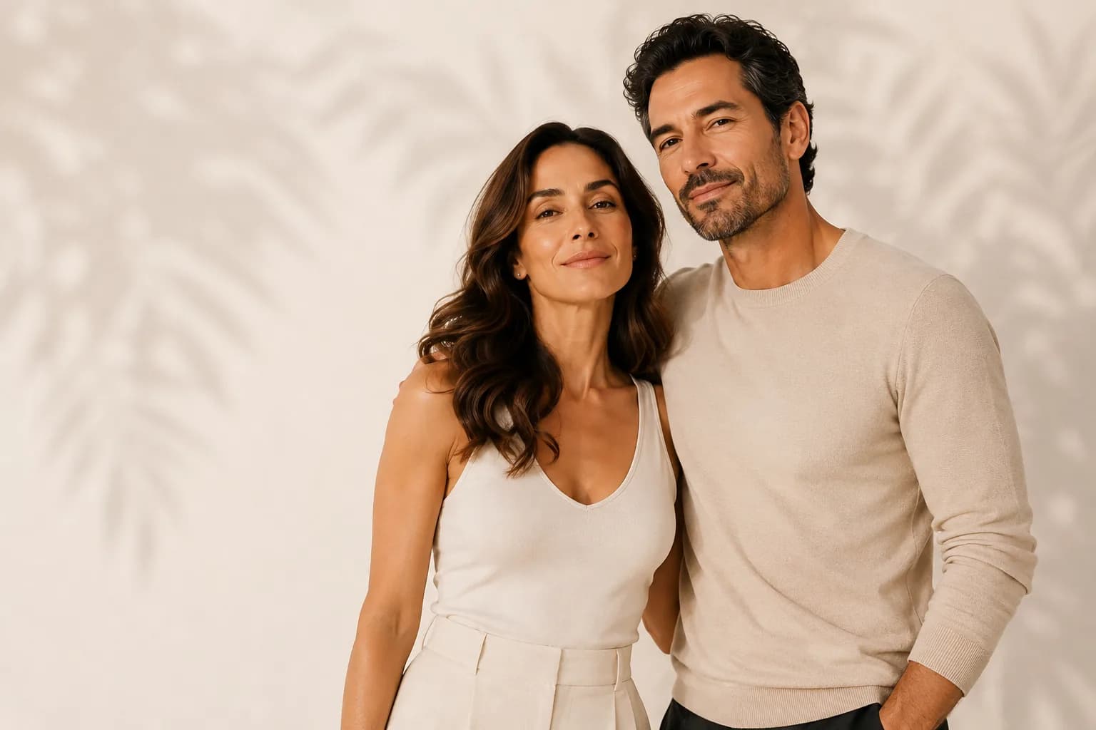 Retrato de una pareja abrazada frente a una pared clara con sombras de hojas.